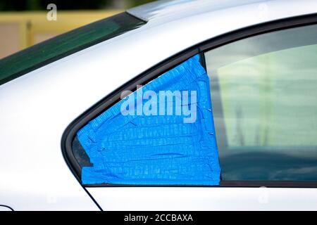 Broken and damaged car window temporarily covered with blue tape to protect interior from rain and water. Smash-and-grab automobile break-ins. Stock Photo