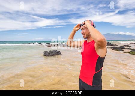 Man triathlete swimmer putting on swim goggles - Triathlon sport athlete going swimming getting ready an ocean swim. Fit man in professional triathlon Stock Photo