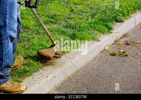 Worker in a gas mower in his hands, mowing grass in front of the house a trimmer in the hands of a man. Stock Photo