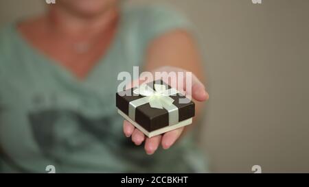 Woman gives  a beautiful small decoartive present gift box tied with golden ribbon, holds it in her hand clsoe up Stock Photo