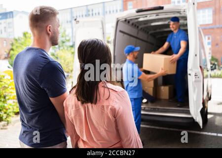 Happy Family Couple Watching Movers Unload Boxes From Truck Stock Photo