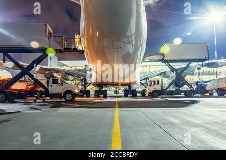 Rear view of the plane during midnight call service at the airport, food trucks on the sides amidst the light of lanterns Stock Photo