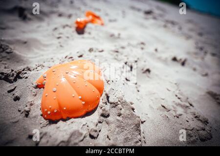 Shallow focus shot of an orange plastic seashell on beach sand Stock Photo