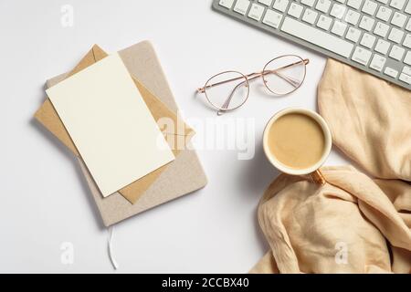 Elegant feminine workspace with pc keyboard, glasses, beige plaid, glasses, blank paper card, envelope, notebook on white background. Flat lay, top vi Stock Photo