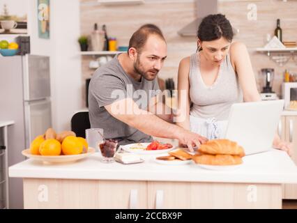 Husband and wife reading a mail on laptop in the morning during breakfast. Married husband and wife in pajamas using internet web online modern technology, smiling and happy in the morning. Reading news browsing internet Stock Photo