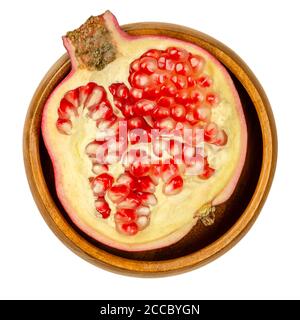 Pomegranate half in a wooden bowl. Split open fruit, Punica granatum, with red to purple seed clusters, made of the sarcotesta, a fleshy seedcoat. Stock Photo