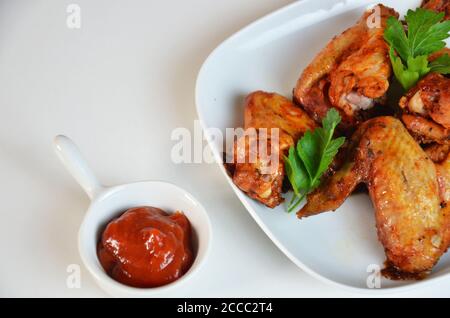 plate of chicken wings on white table red sauce in a gravy boat Stock Photo