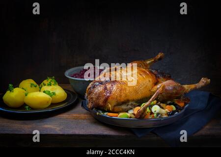 Roasted duck with potatoes and red cabbage, a festive meal on a rustic wooden table, dark brown background with copy space, selected focus, narrow dep Stock Photo