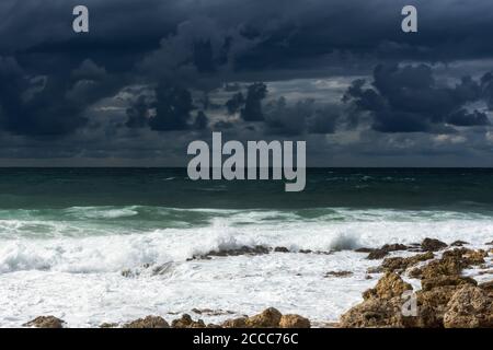 A violent storm in the sea. Beautiful blue storm clouds. A cloudy, menacing landscape. A terrible storm warning. Waves break on the rocky shore. Stock Photo