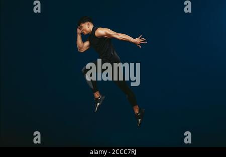 Sports man doing jumping and stretching workout. Full length of healthy fitness man doing exercise over dark background. Stock Photo