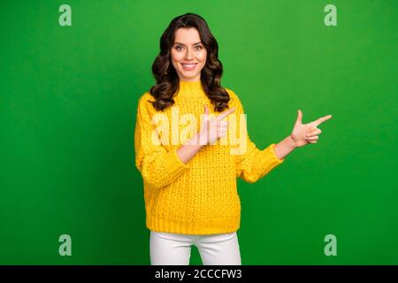 Photo of funny pretty lady hold hands directing fingers empty space advising cool offer novelty wear knitted yellow pullover white trousers isolated Stock Photo