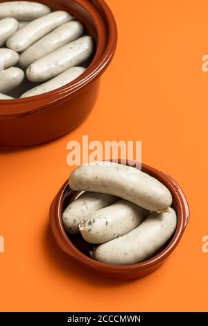 Eating white sausage in a ceramic plate, on an orange seamless background. German veal sausage boiled and ready to eat. Traditional German food. Stock Photo