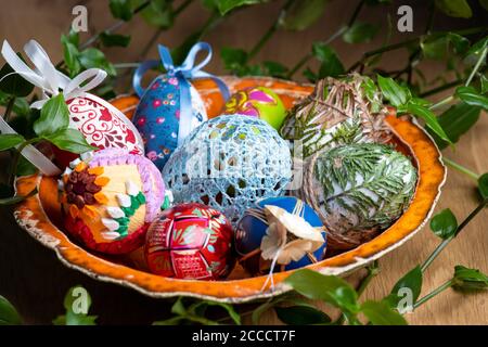 Easter eggs decorated with a different techniques in a beautiful orange bowl surrounded by green leafs. Stock Photo