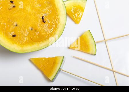 Pieces of yellow watermelon on sticks. Plate on a white surface. Stock Photo