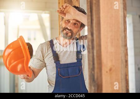 Smiling man in overalls holding his helmet Stock Photo