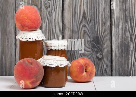 Jam in glass jars. Peaches lie nearby. Jam in glass jars. Peaches lie nearby. Against a background of painted pine planks.. Stock Photo