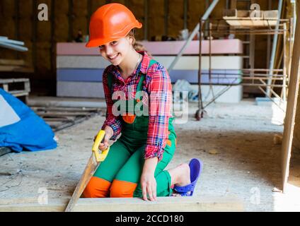 little girl working with wood. kid sawing a plank in carpentry. working with wood in a garage. happy childhood. hardworking child sawing with hand wood saw. teenage girl with hand-saw. Stock Photo