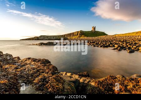 Dunstanburgh Castle shot early morning with the North Sea lapping in the bay. Stock Photo