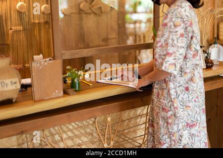 Woman client signing hotel contract paper at reception desk In face mask. Stock Photo