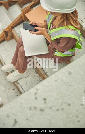 Woman in a hard hat using her smartphone Stock Photo