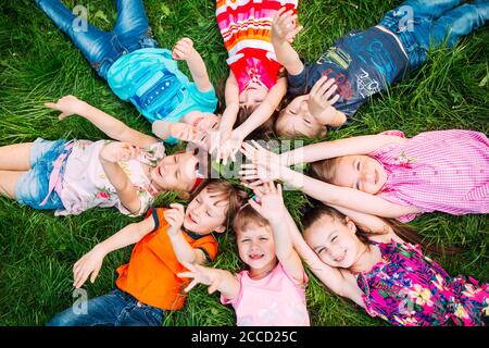A group of children lying on the green grass in the Park. The interaction of the children. Stock Photo