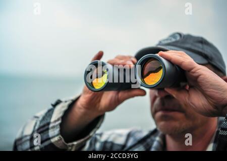 Close up shot of man looking through binoculars with not visible face. Stock Photo