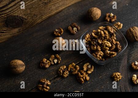 Walnut in a smale plate with scattered shelled nuts and whole nut which standing on a wooden vintage table. Walnuts is a healthy vegetarian protein Stock Photo