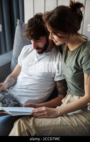 Lovely young couple relaxing on a couch at home, reading magazine Stock Photo