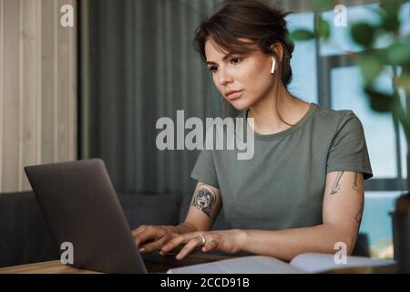 Attractive pensive young woman working on laptop computer while sitting at the table at home Stock Photo