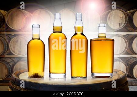 4 bottles of glowing amber whisky, in various shapes, set on top of an old barrel, in a barrel warehouse, back lit with colourful lens flare. Stock Photo
