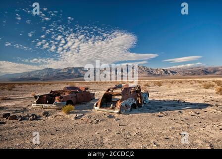 Old car wrecks, riddled with bullets, at Four Mine Road in Panamint Valley, Inyo Mountains in distance, Death Valley National Park, California, USA Stock Photo