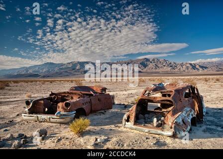 Old car wrecks, riddled with bullets, at Four Mine Road in Panamint Valley, Inyo Mountains in distance, Death Valley National Park, California, USA Stock Photo