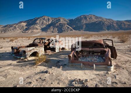 Old car wrecks, riddled with bullets, at Four Mine Road in Panamint Valley, Inyo Mountains in distance, Death Valley National Park, California, USA Stock Photo