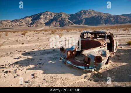 Old car wreck, riddled with bullets, at Four Mine Road in Panamint Valley, Inyo Mountains in distance, Death Valley National Park, California, USA Stock Photo