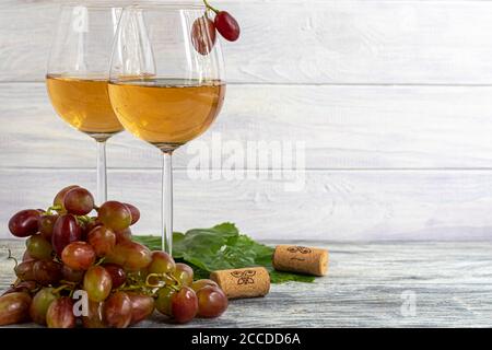 Large and light, wine grapes. It is covered with a white coating called yeast. Glasses are filled with light wine. Water drops on berries. On a wooden Stock Photo