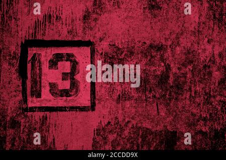 number 13 painted with black stencil on stained red concrete wall Stock Photo