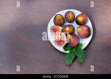 A plate full of fresh figs, one of them cut in halves, decorated with fig leave on wooden table Stock Photo