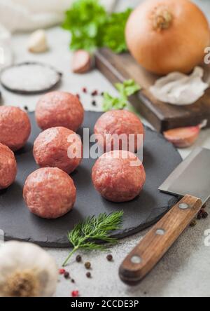 Fresh raw meatballs on stone board with pepper, salt and garlic on light table background with dill,parsley and dill. Top view Stock Photo
