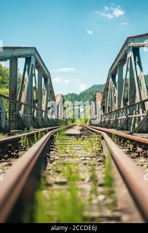 Railway bridge over river in Polish mountain. Heavy rusty steel old industrial train overpass in natural scenic landscape, blue summer sky. Stock Photo