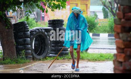 An Indian old man walking in the pouring rain in the small village. Stock Photo