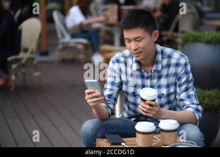 Medium shot one young Asian man using phone at outdoor cafe. blur background Stock Photo