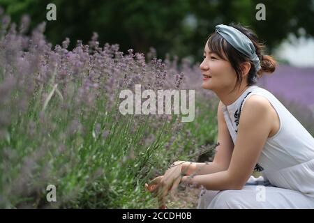 One beautiful Asian young woman squatting at lavender bush, smiling. Blur background Stock Photo