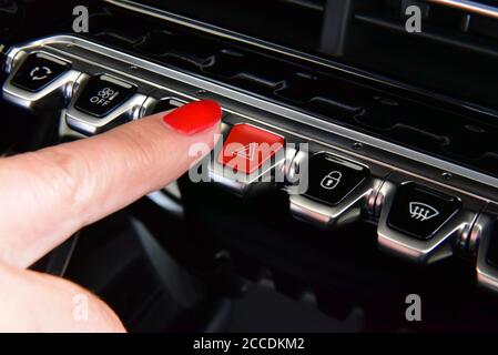 Woman pressing red triangle car hazard warning button. Female finger hitting car emergency light botton. Stock Photo