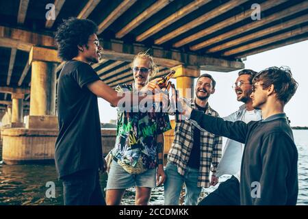 Group of friends celebrating, resting, having fun and party in summer day. Young men drinking beer, talking, laughting. Look happy and cheerful. Festive time, holiday, summertime, unity and friendship.
