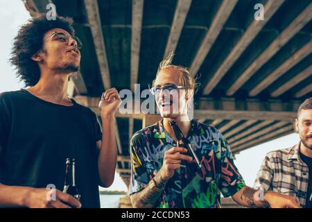 Group of friends celebrating, resting, having fun and party in summer day. Young men drinking beer, talking, laughting. Look happy and cheerful. Festive time, holiday, summertime, unity and friendship. Stock Photo