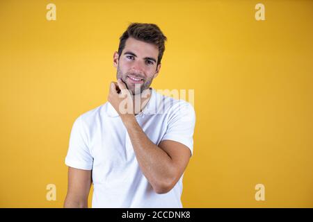 Young handsome man over yellow background touching beard looking at the camera Stock Photo