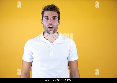 Young handsome man standing over insolated yellow background surprised and amazed Stock Photo