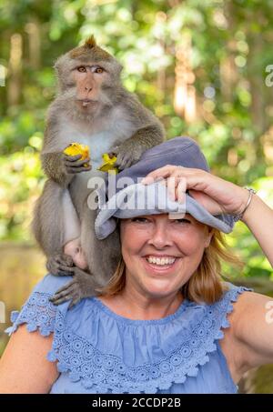 Vertical portrait of a female tourist with a macaque sitting on her shoulder in Bali. Stock Photo