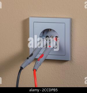 measuring voltage in modern wall plug with red and black leads Stock Photo