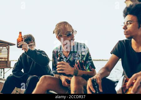 Group of friends celebrating, resting, having fun and party in summer day. Young men drinking beer, talking, laughting. Look happy and cheerful. Festive time, holiday, summertime, unity and friendship. Stock Photo